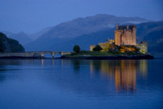 A typical photo of Eileen Donan castle, taken at dusk with the castle lit up and reflected in the water.